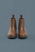 Brown waterproof Chelsea boots with water droplets on a blue-grey background